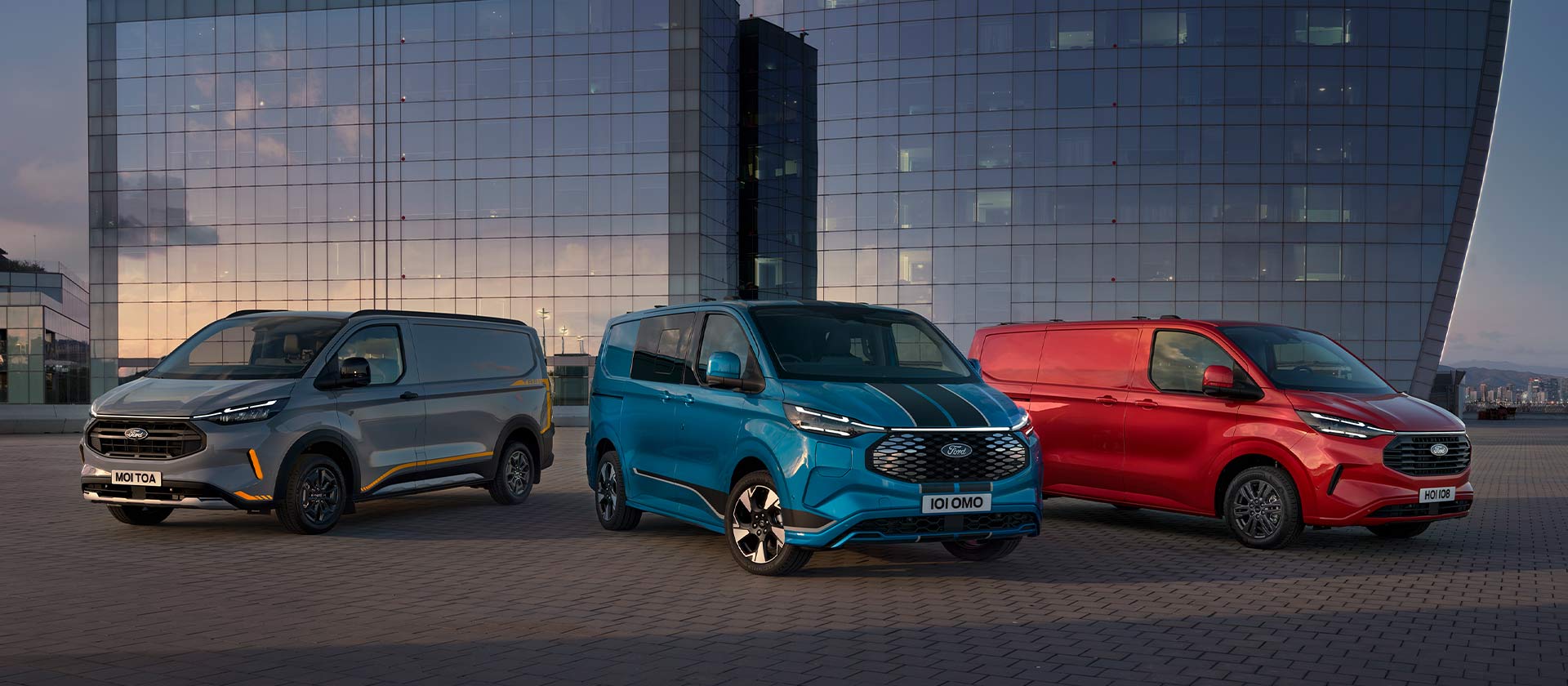 Trois fourgonnettes Ford Transit Custom Sport garées en gris, bleu et rouge.