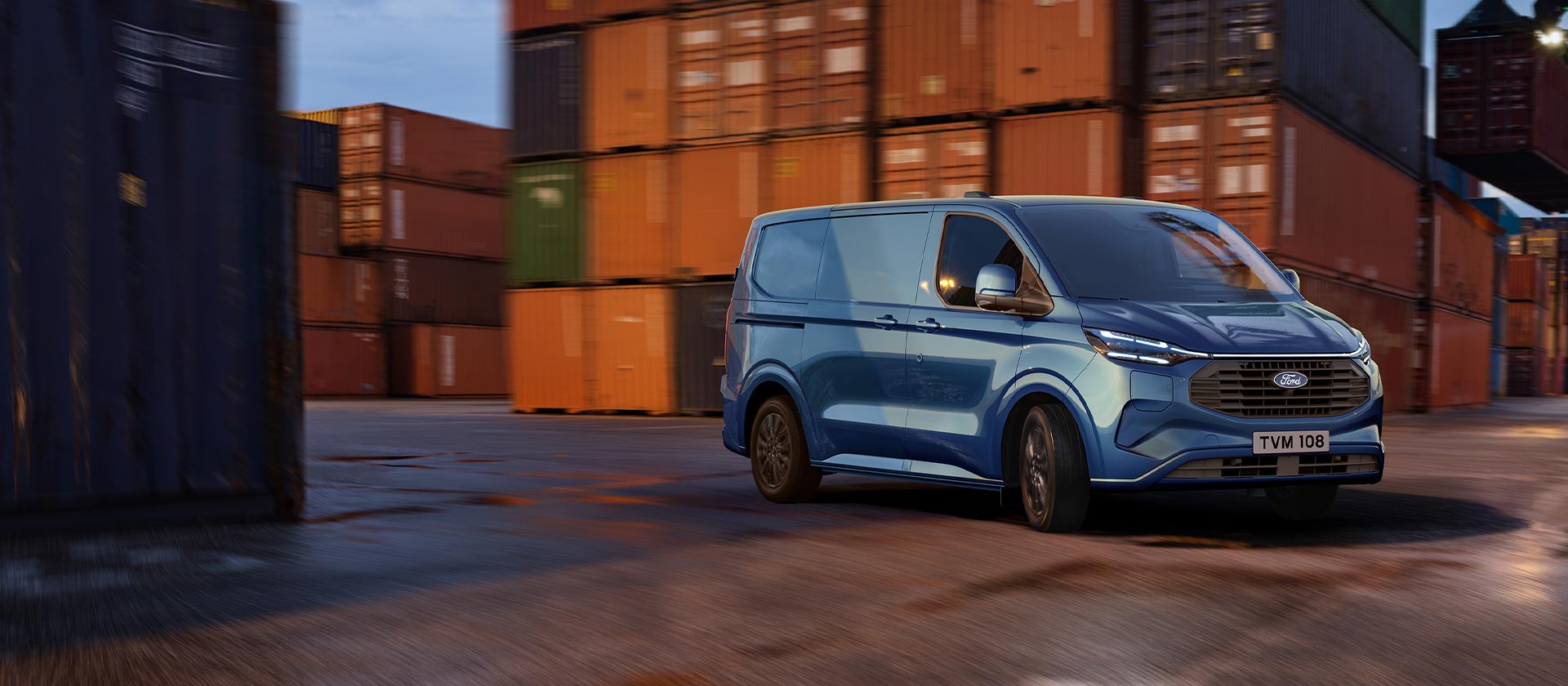 Une camionnette Ford Transit Custom bleue circule dans une zone portuaire.