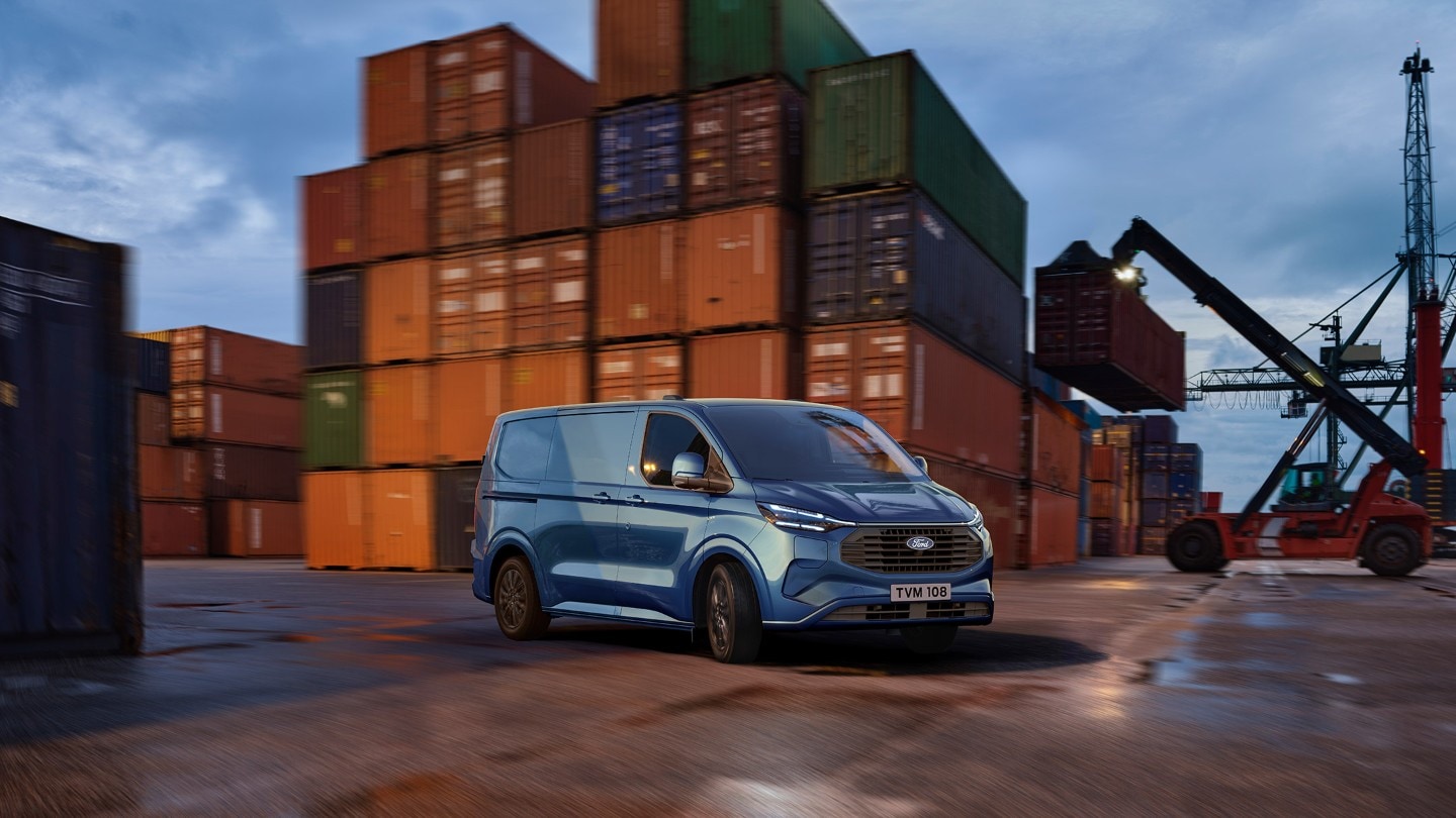  Ford Transit Custom Plug-In Hybrid bleu dans un terminal à conteneurs au crépuscule.