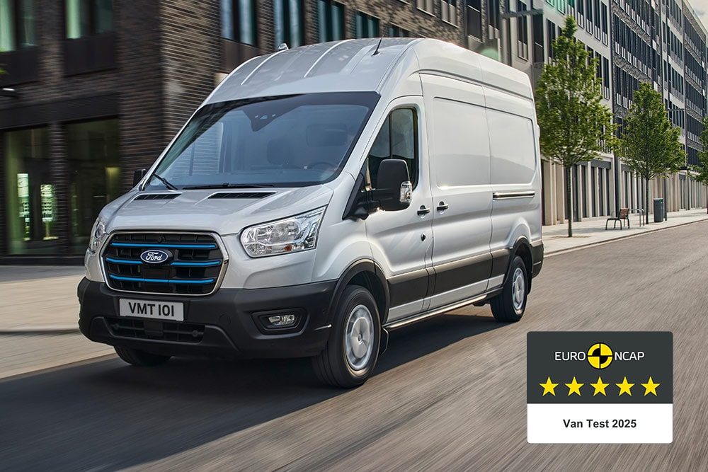 Fourgon électrique Ford E-Transit argenté circulant sur une route, avec un badge « Gold 2022 Commercial Van Safety ».