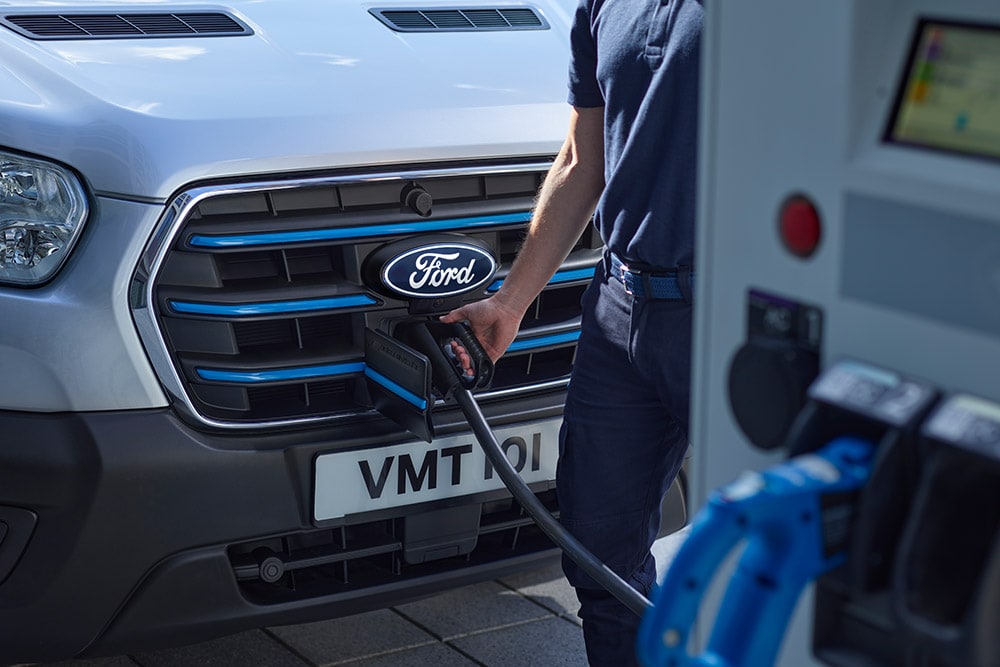 Gros plan d'une personne branchant un câble de recharge dans un fourgon électrique Ford E-Transit argenté.