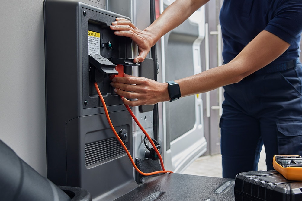 Gros plan d'une personne branchant un câble de recharge à l'intérieur d'un fourgon électrique Ford E-Transit.
