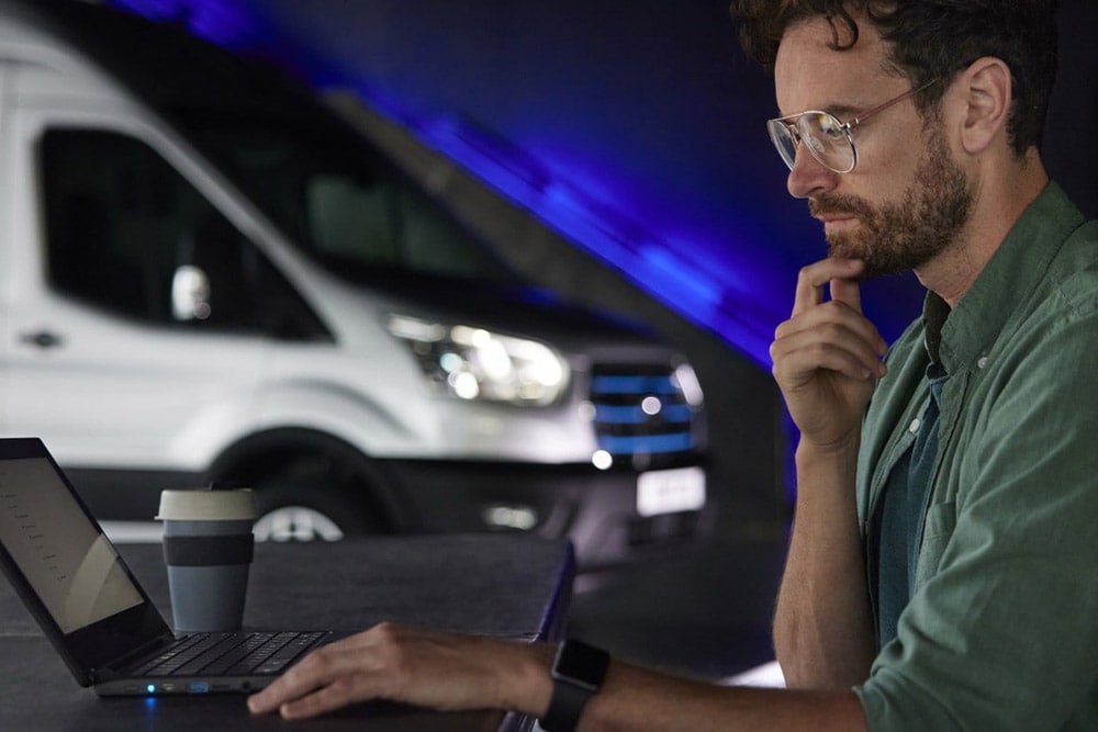 Homme travaillant sur un ordinateur portable avec un fourgon Ford E-Transit en arrière-plan.