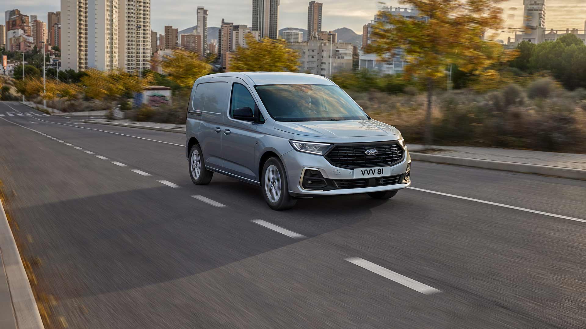Ford Transit Connect circulant en ville, montrant les enjoliveurs de phares antibrouillard chromés et les phares automatiques.