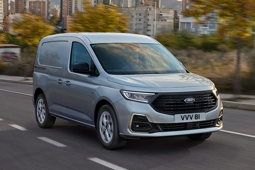 Ford Transit Connect circulant en ville, montrant les enjoliveurs de phares antibrouillard chromés et les phares automatiques.