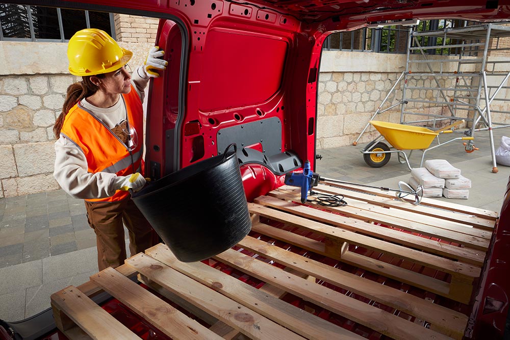 Une femme place du matériel de construction dans l'espace de chargement d'un Ford Transit Connect avec les portes latérale et arrière ouvertes.