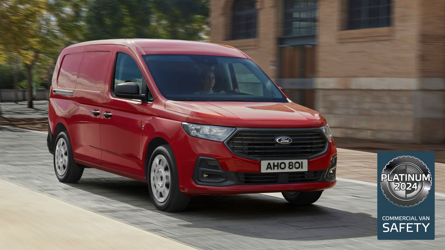 Un Ford Transit Connect en Maple Red avec calandre et phares automatiques roule sur une route. 