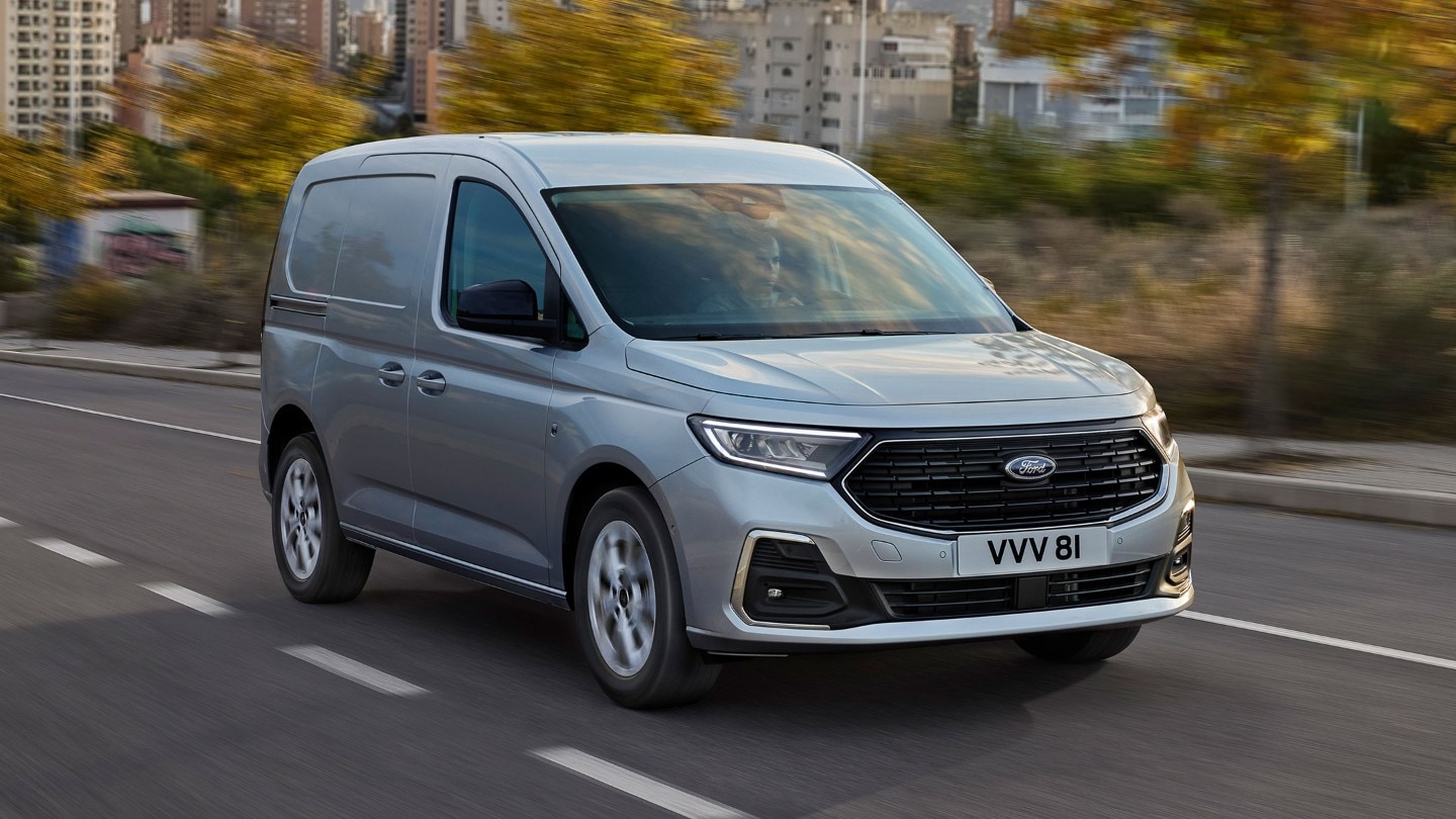 Le Ford Transit Connect Limited en Stardust Silver, avec baguettes chromées et phares automatiques, roule sur une route. 