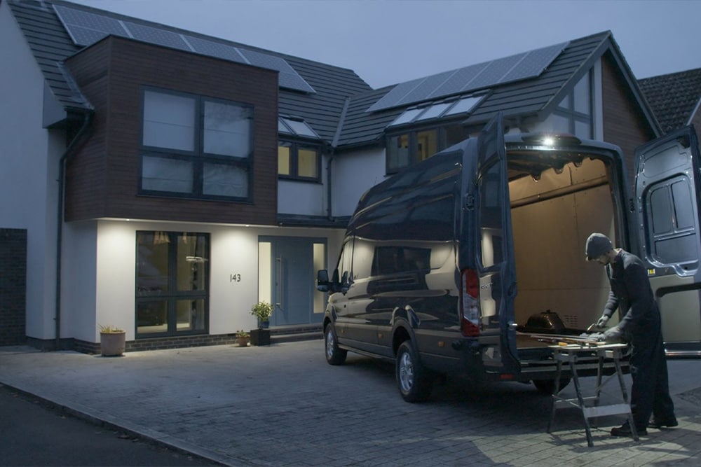 Un charpentier travaille de nuit à l'arrière d'un Ford Transit Fourgon, portes arrière ouvertes. Il est éclairé par l'éclairage extérieur à LED.