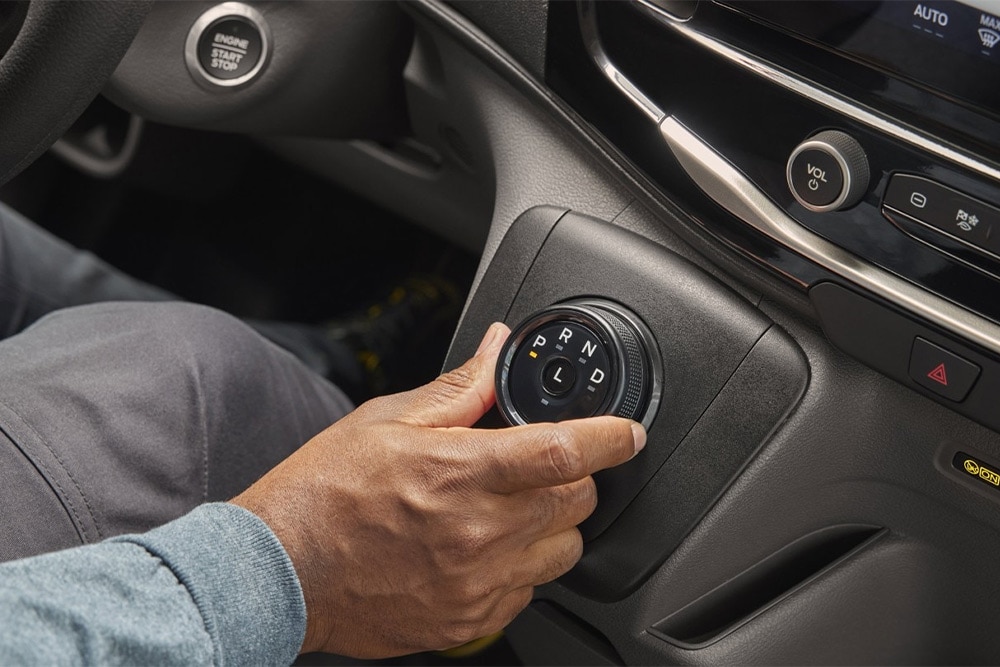 Une main actionne le sélecteur rotatif de vitesse sur la console centrale du Ford Transit Fourgon.