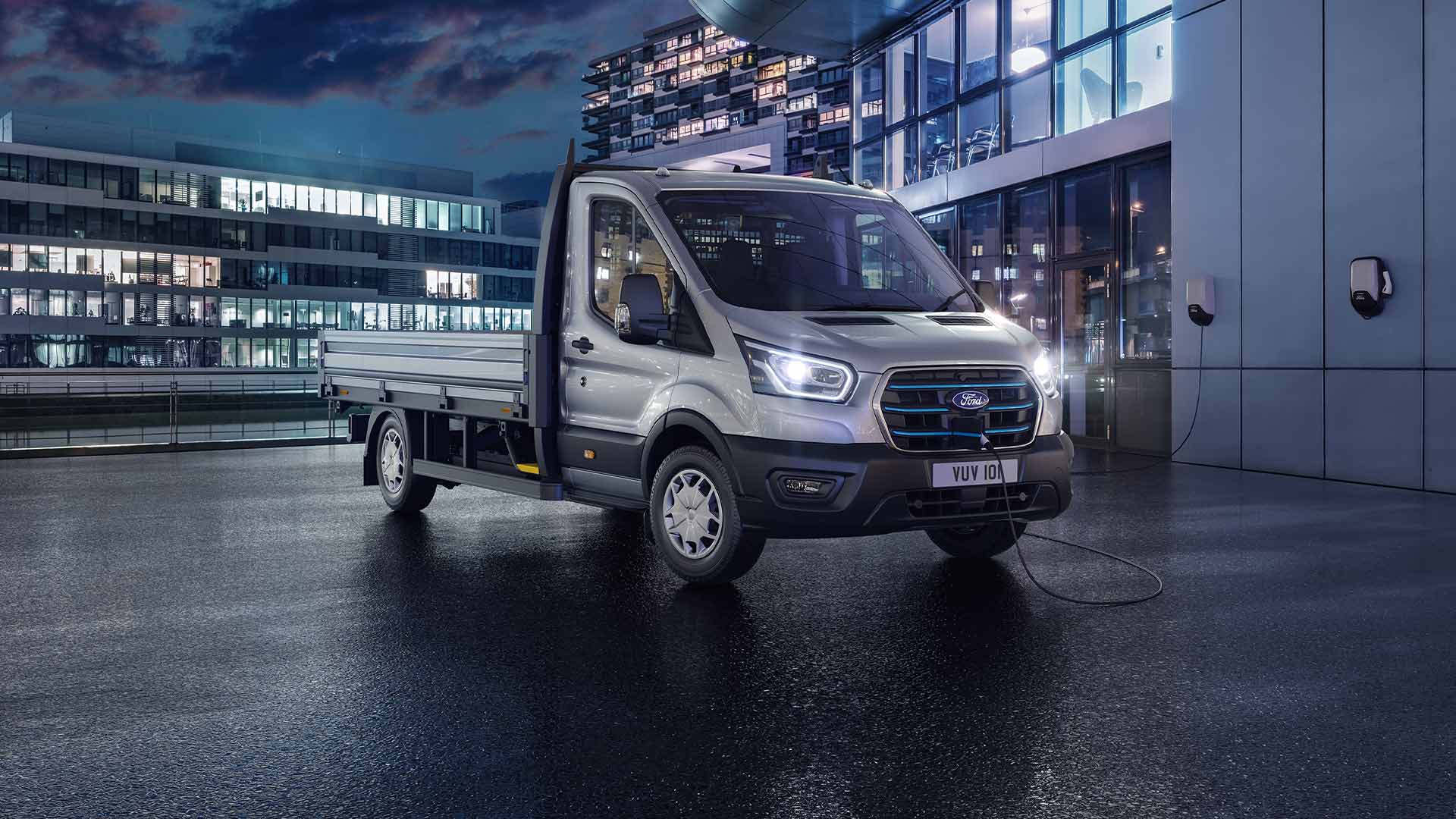 Châssis-cabine argenté Ford Transit garé devant un bâtiment moderne la nuit.