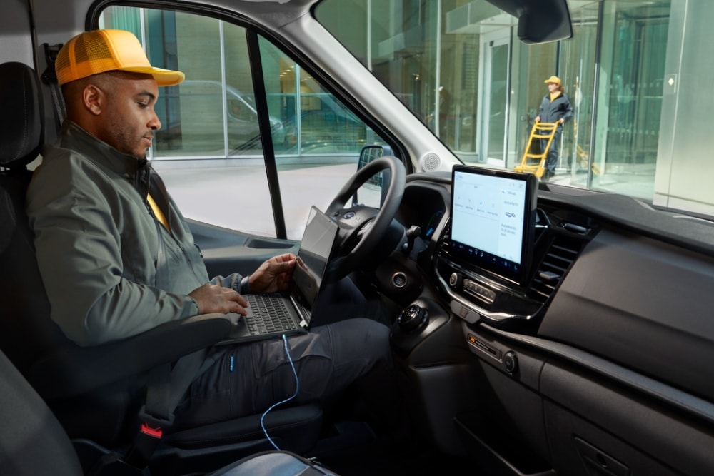 Homme assis sur le siège conducteur d’un fourgon Ford Transit, utilisant un ordinateur portable.