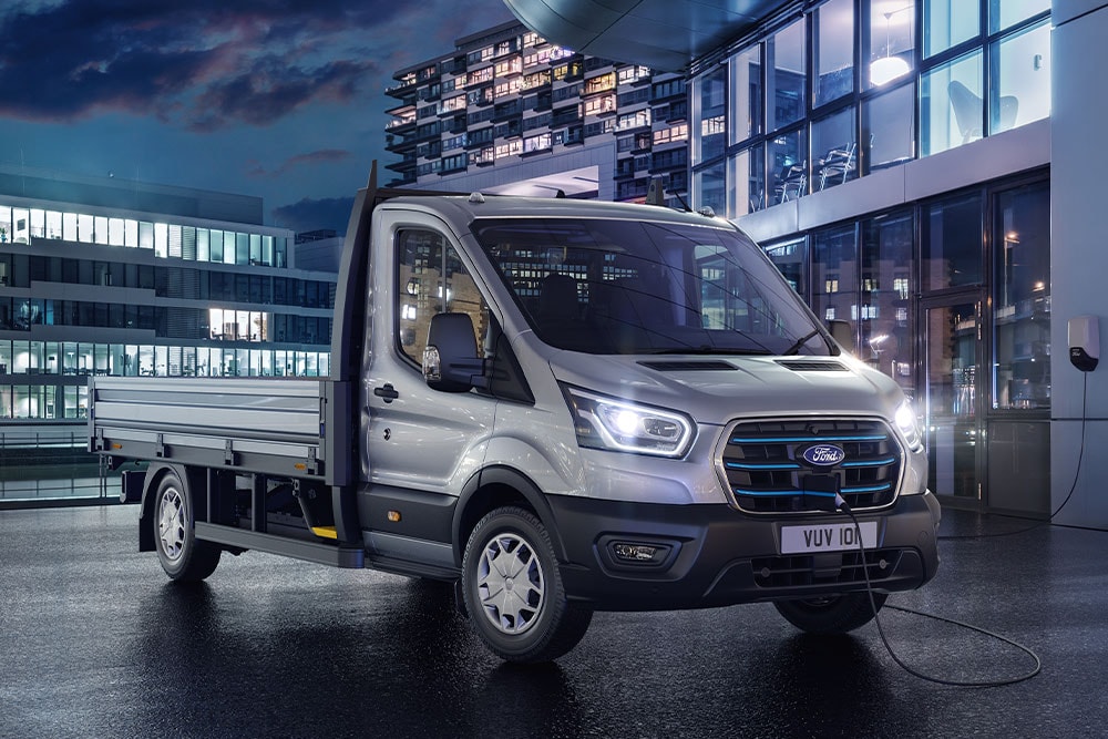 Châssis-cabine argenté Ford Transit garé devant un bâtiment moderne la nuit.