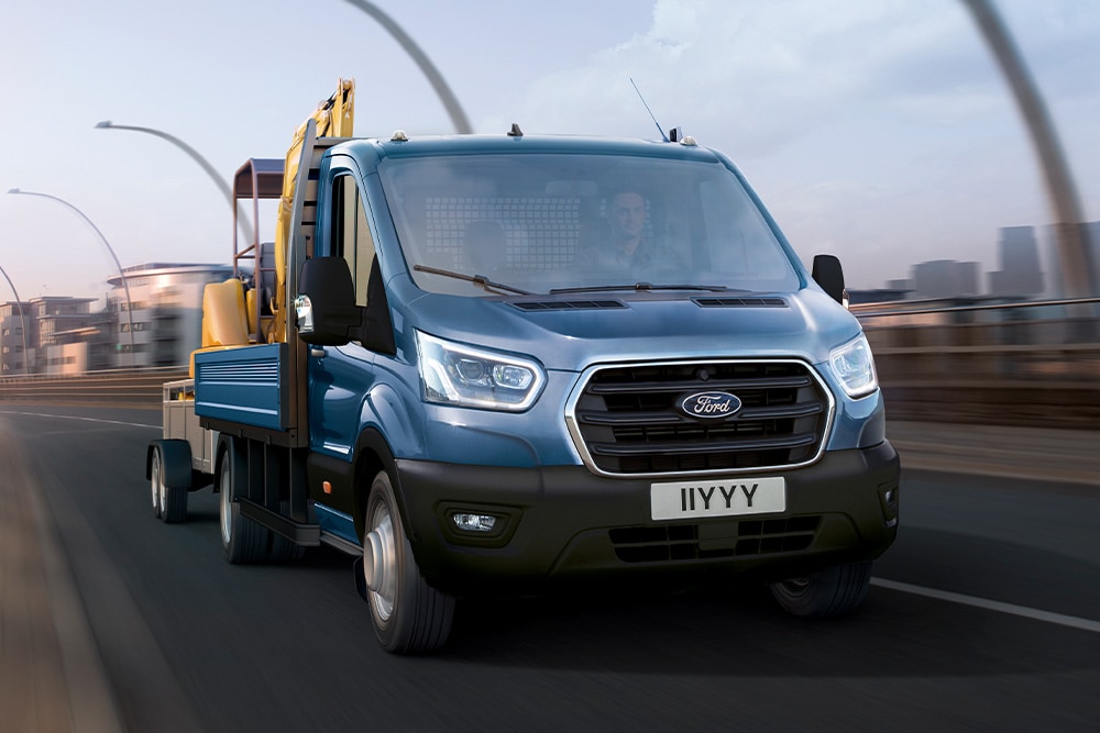 Vue de la calandre du châssis cabine Ford Transit transportant une pelleteuse en circulant en ville. 