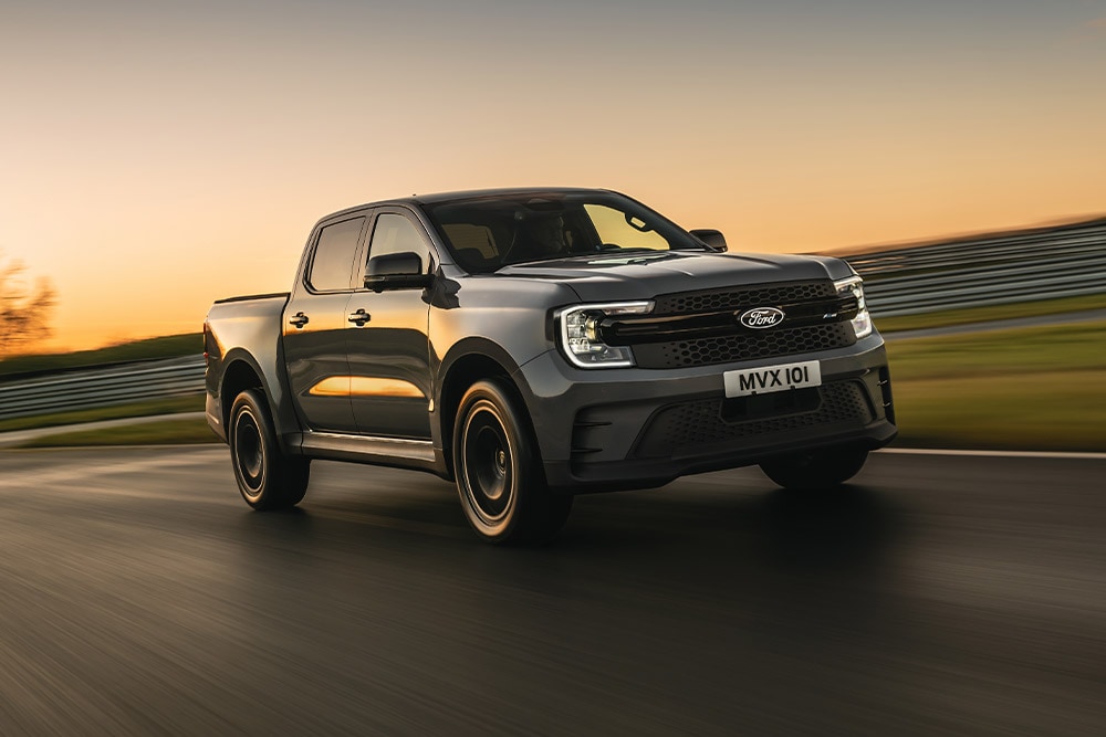 Un Ford Ranger Platinum gris foncé roule sur une piste au coucher du soleil.