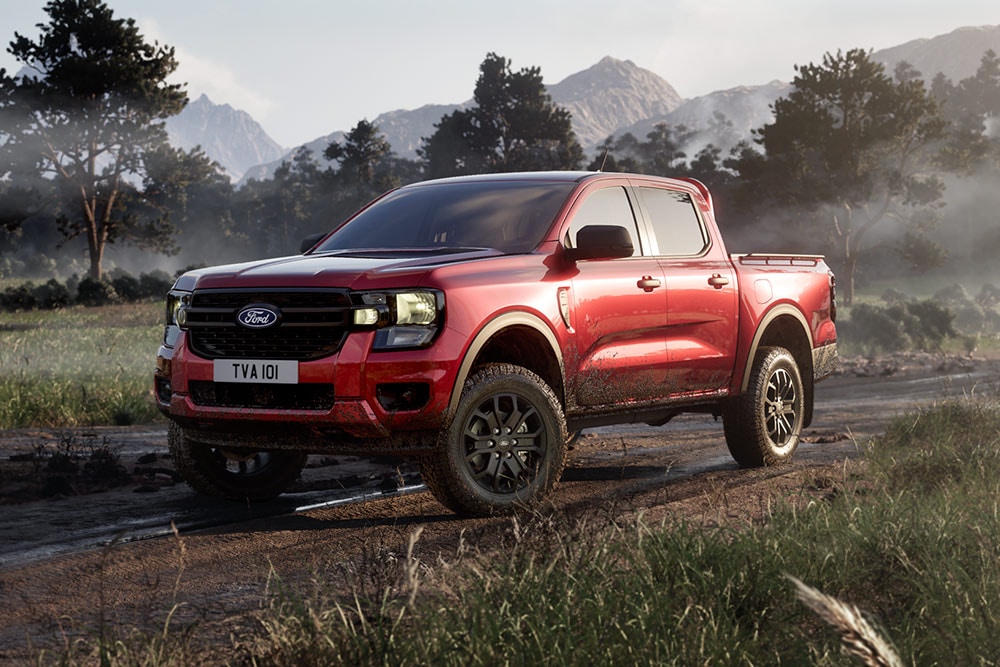 Un Ford Ranger Raptor rouge roulant sur un chemin de terre dans un paysage pittoresque.