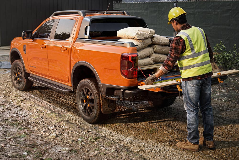 Ouvrier du bâtiment chargeant de l’équipement dans la benne d’un Ford Ranger orange.