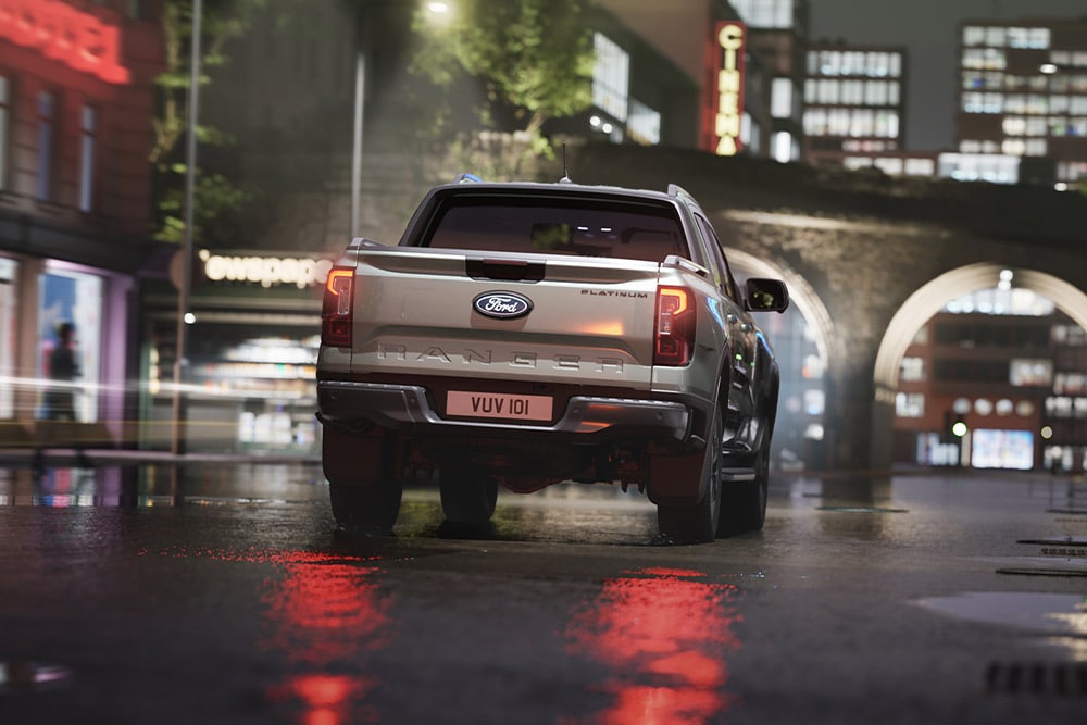 Vue arrière d'un Ford Ranger argenté roulant dans un paysage urbain éclairé au néon la nuit.