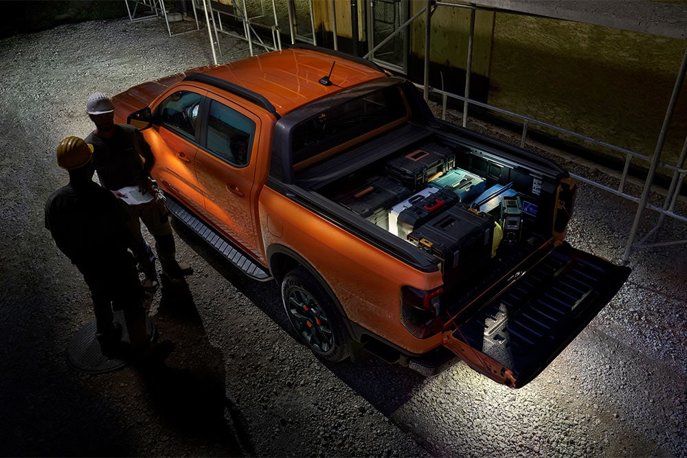 Vue aérienne du Ford Ranger Wildtrak orange de nuit, avec l’éclairage de zone extérieure.