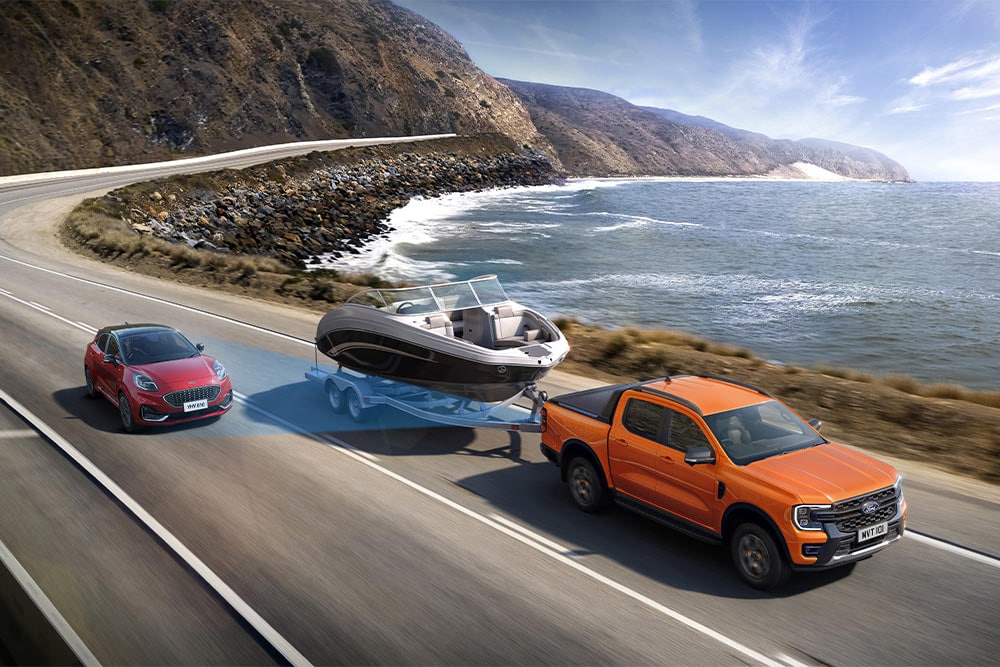 Un Ford Ranger orange remorque un bateau sur une route côtière, démontrant sa capacité de remorquage.