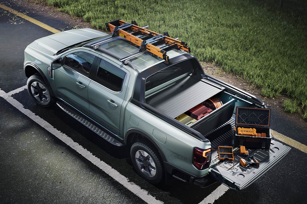 Vue arrière en plongée d'un pick-up Ford Ranger gris, avec benne ouverte, outils et galerie de toit sur une surface pavée. 