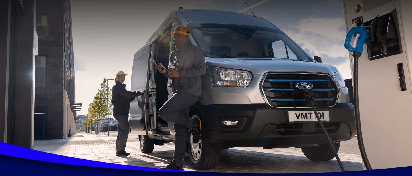 Deux ouvriers chargent un Ford E-Transit argenté vu de face