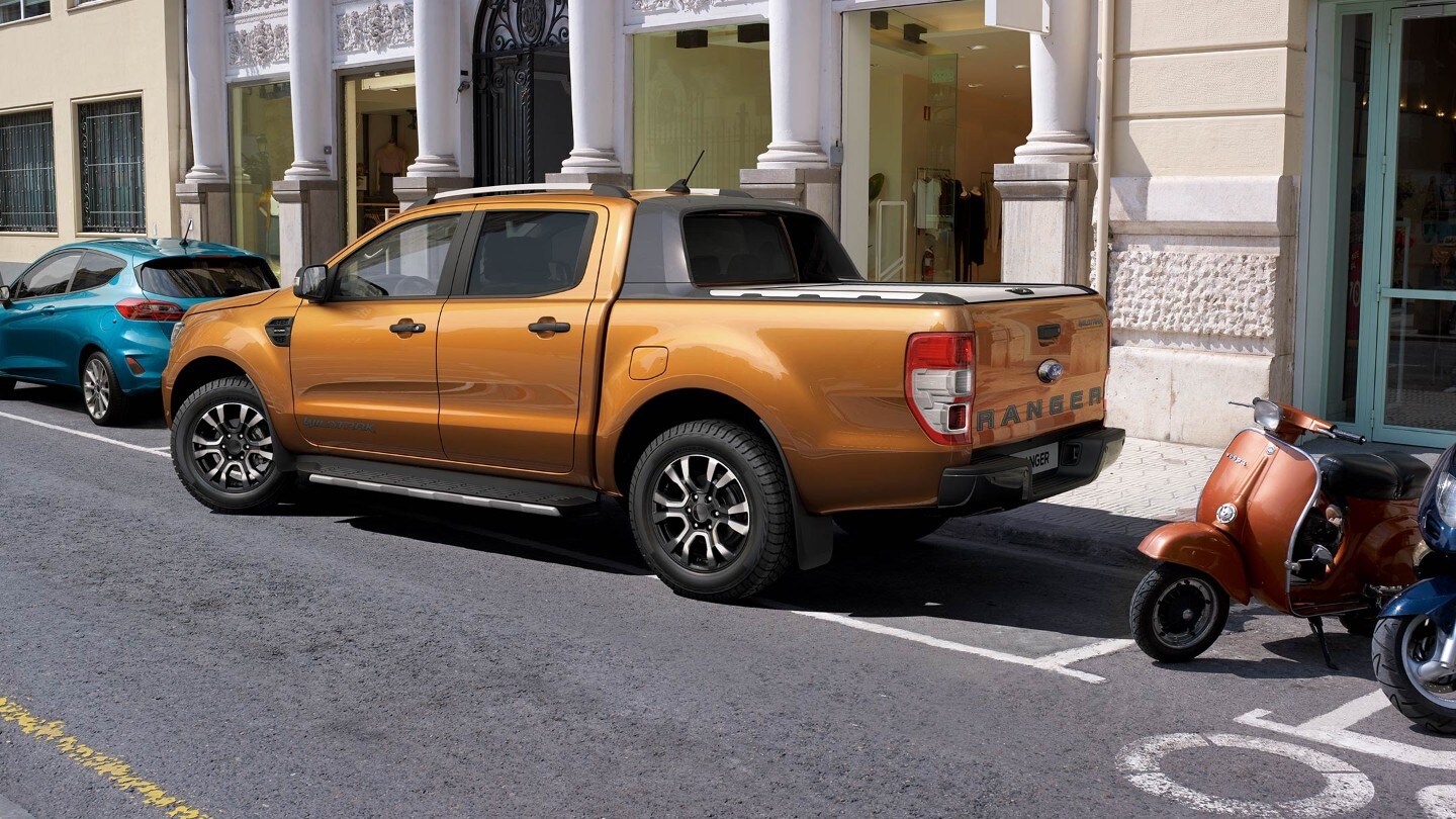 Ford Ranger couleur orange, vue latérale aux trois quarts, se garant dans une place de parc sur le côté.