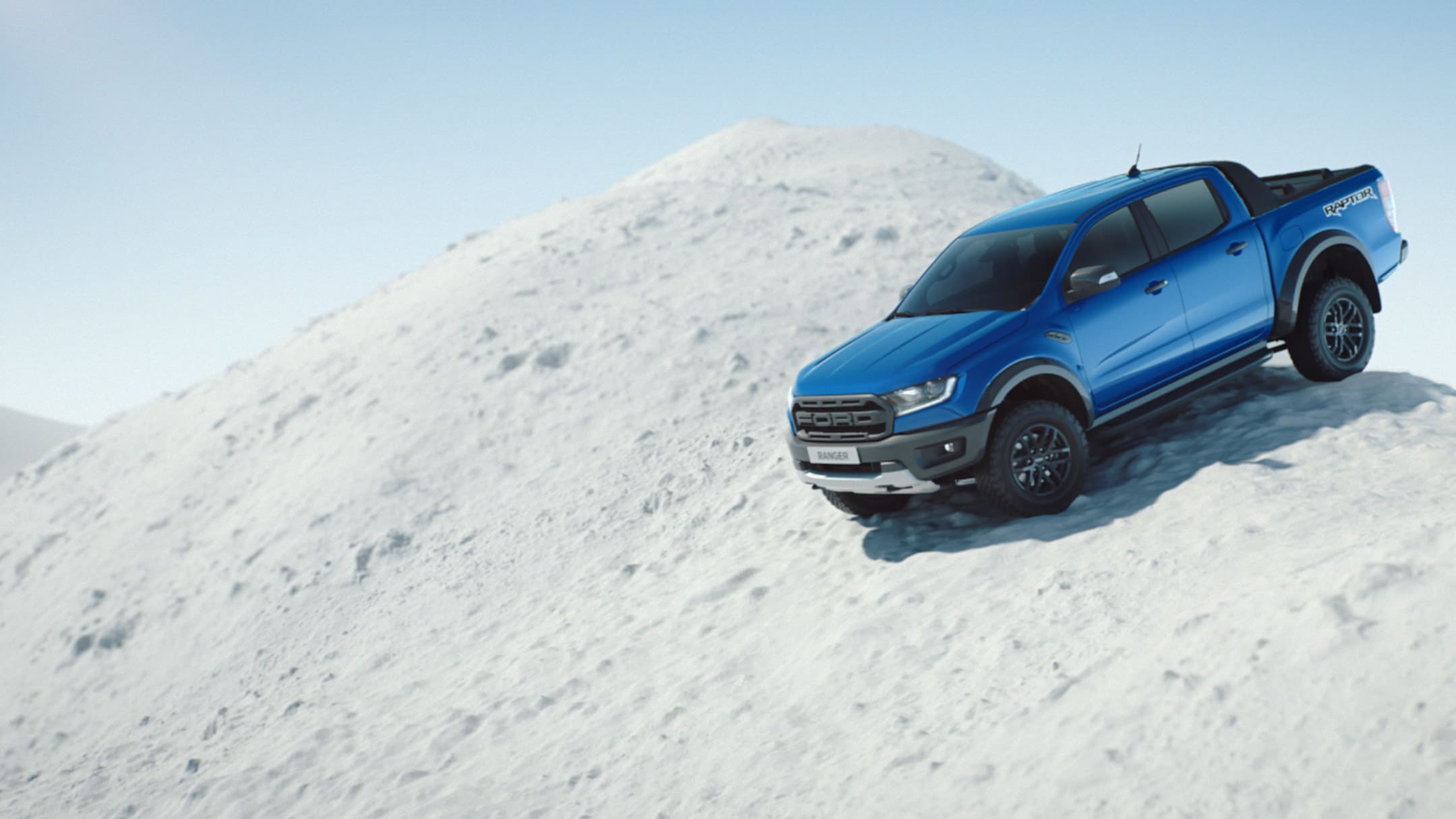 Ford Ranger bleu ¾ vue latérale en descente en mouvement sur le sommet d'une montagne enneigée