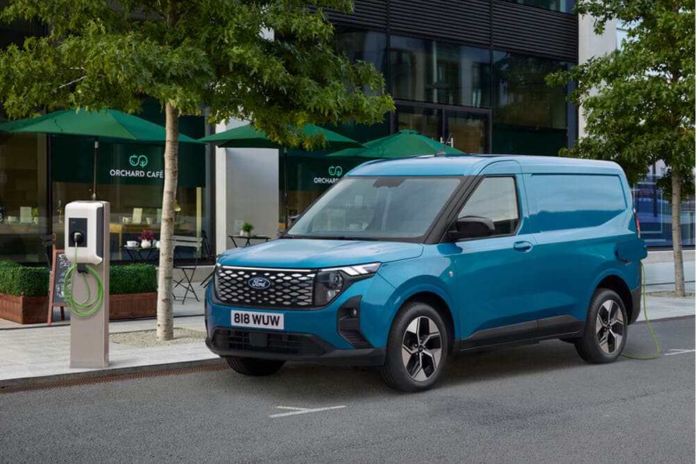 Ford E-Transit Courier bleu vu de trois quarts avant, garé près d'une borne de recharge