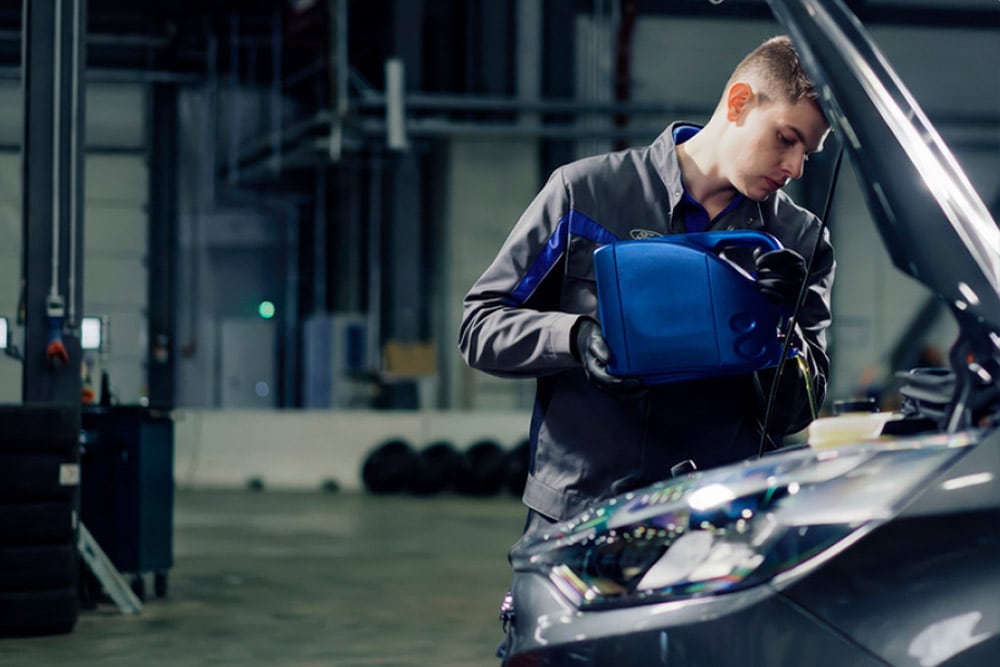 Vue latérale d'un technicien agréé Ford effectuant des réparations sur un véhicule dans un garage.