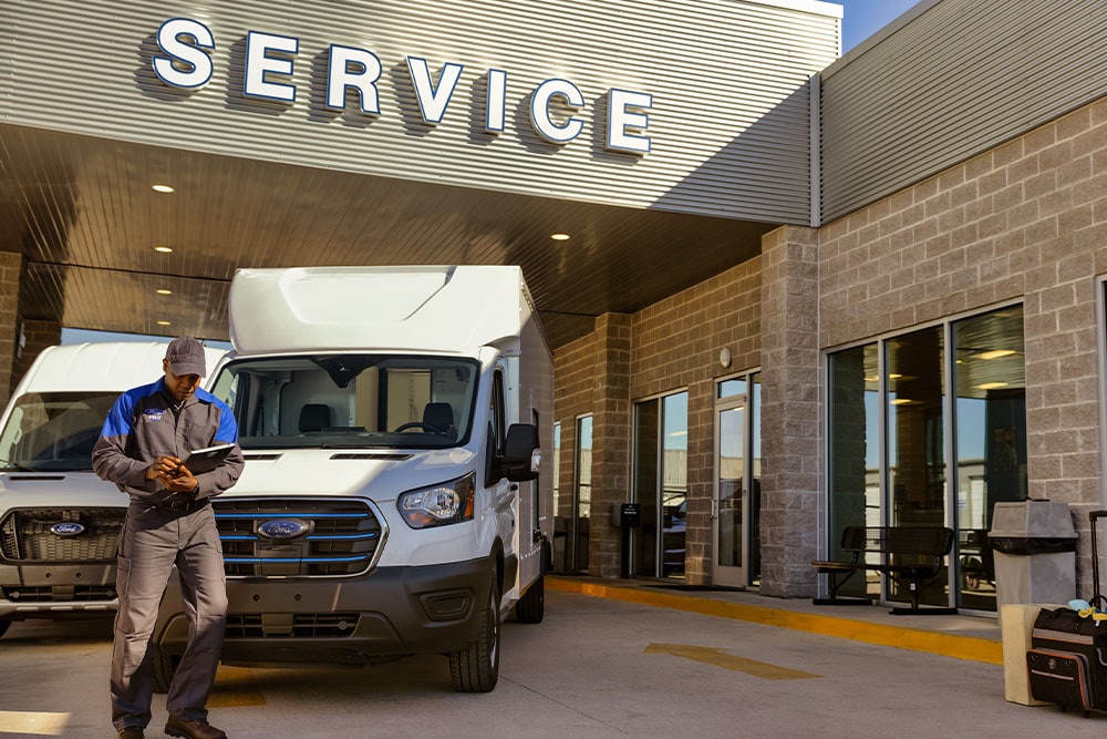 Mécanicien Ford debout devant une camionnette Ford blanche près d'un bâtiment étiqueté "service".
