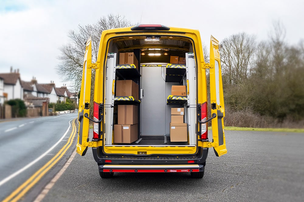 Vue arrière d'une camionnette Ford Transit jaune avec les portes ouvertes, révélant un intérieur organisé avec des étagères et des boîtes.