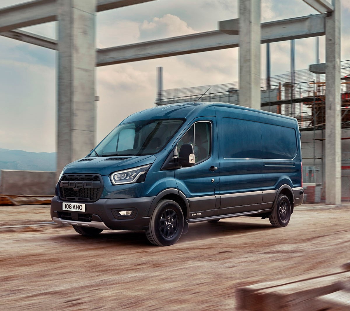 Ford Transit bleu vu de côté traversant un chantier de construction