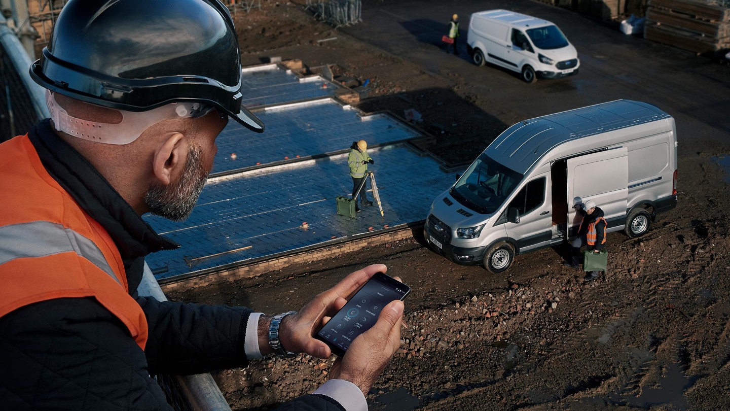 Un ouvrier portant un casque de chantier regarde un véhicule d'entreprise depuis un bâtiment