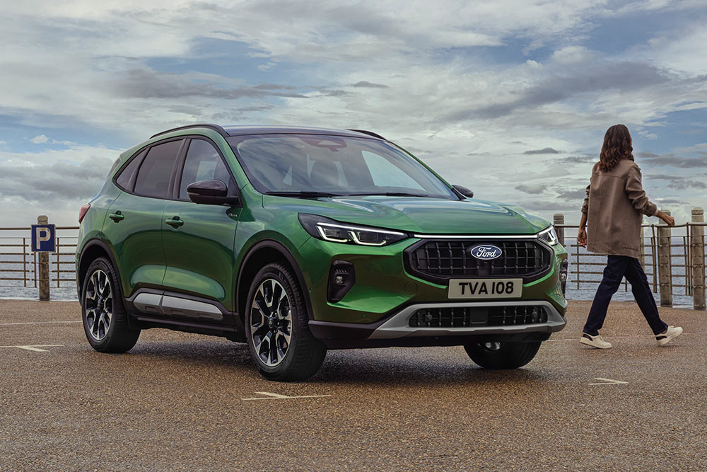 Une Ford Kuga verte garée en bord de mer, vue de trois quarts avant, avec une personne marchant à proximité.