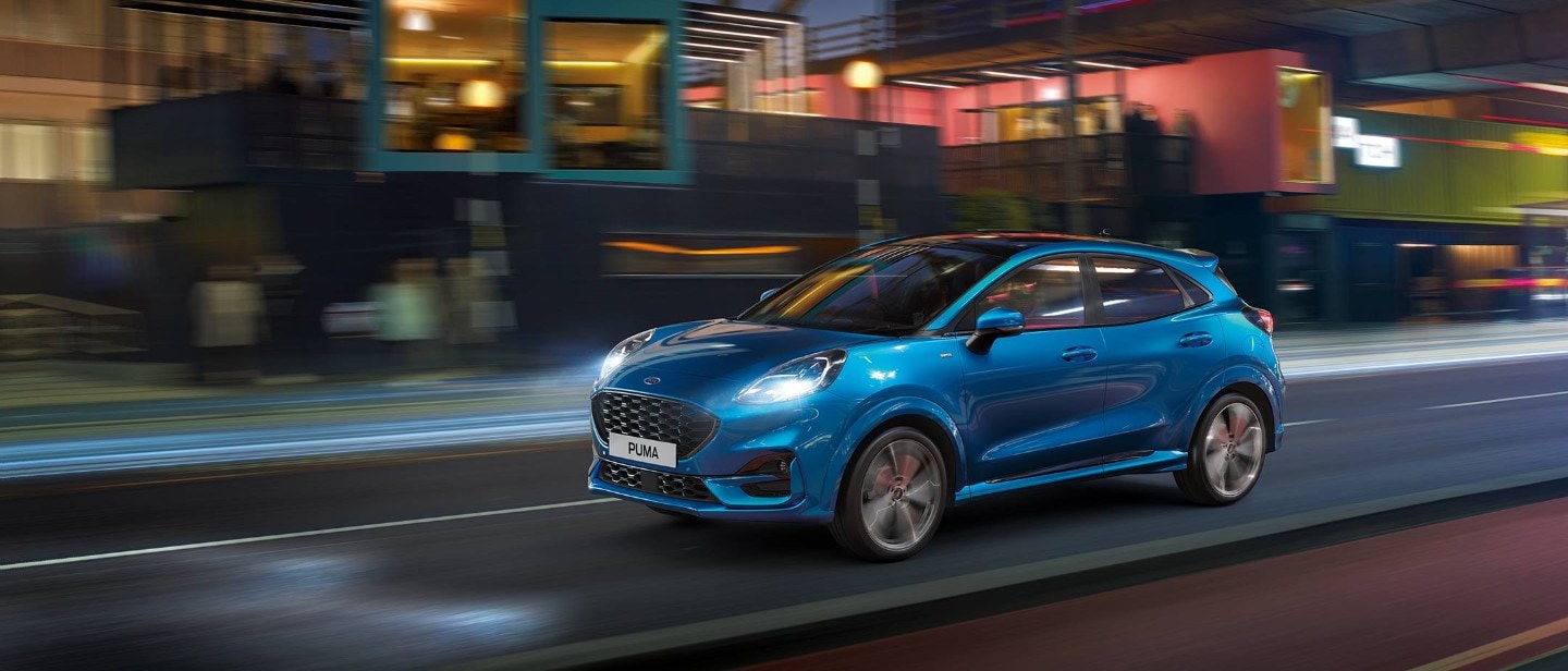 image of a Blue Ford Puma driving on an empty road.